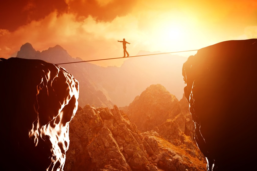 Man walking and balancing on rope over precipice in mountains